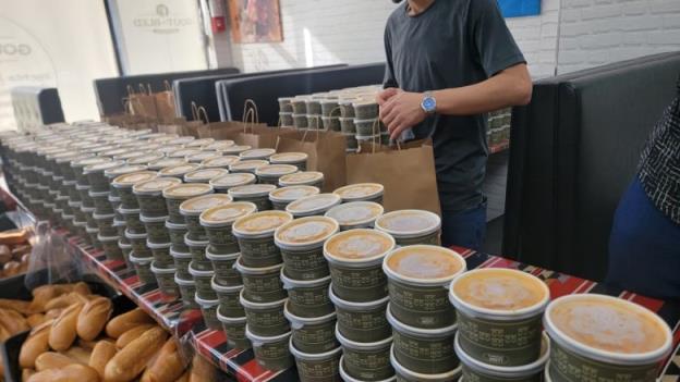 Smiling people are working near tables filled with individually packaged foods.