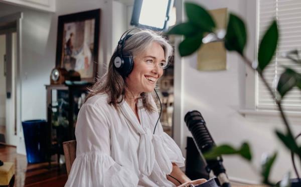 Petra sits at a desk with headpho<em></em>nes on, speaking into a microphone and smiling.
