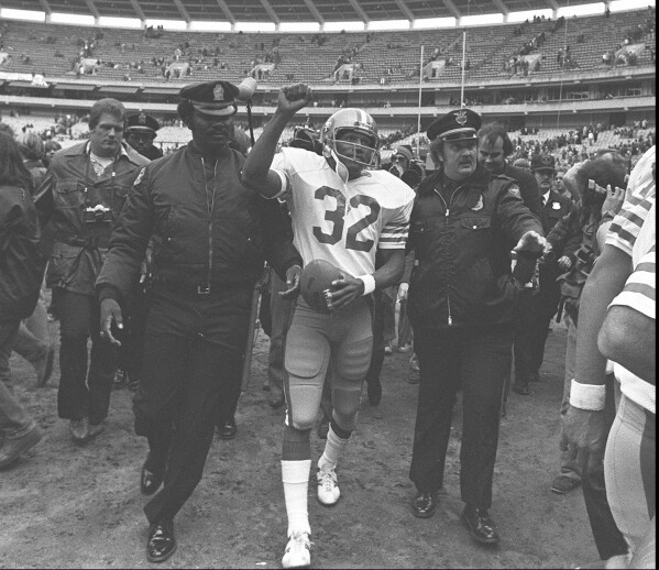 FILE - San Francisco 49ers running back O.J. Simpson is escorted from the field by police after the final NFL football game of his career, Dec. 16, 1979, against in the Atlanta Falcons at Atlanta Fulton County Stadium in Atlanta, Ga. Simpson, the decorated football superstar and Hollywood actor who was acquitted of charges he killed his former wife and her friend but later found liable in a separate civil trial, has died. He was 76. (AP Photo, File)