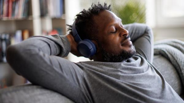 Young man enjoying music over headpho<em></em>nes while relaxing on the sofa at home. Pic: iStock