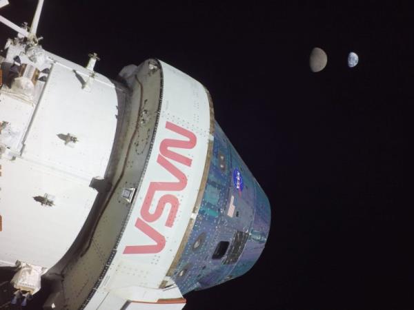 Sunlit front end of space capsule labeled NASA, with tiny Earth and moon in distance.