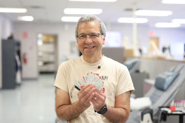 henry bickoff with grey hair and glasses stands with a series of blood do<em></em>nor cards splayed in his hands.