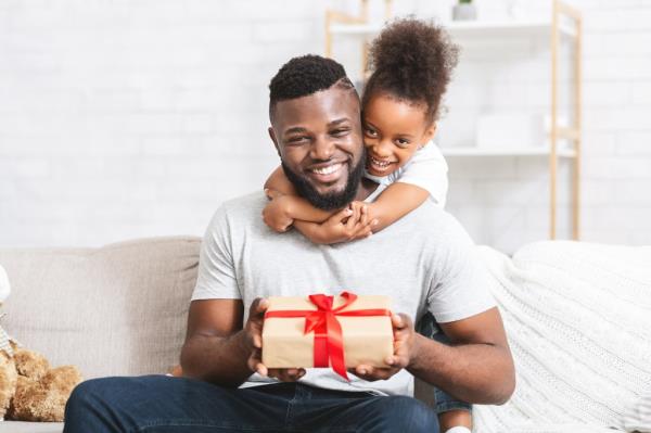 A little girl hugs her father's neck from behind as he holds a Father's Day gift.