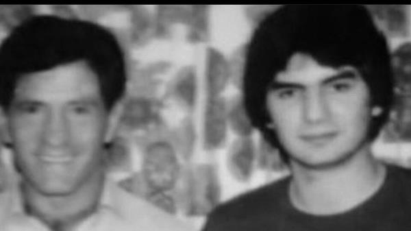 Michael Franzese in a suit and glasses being surrounded by men at a dinner table.