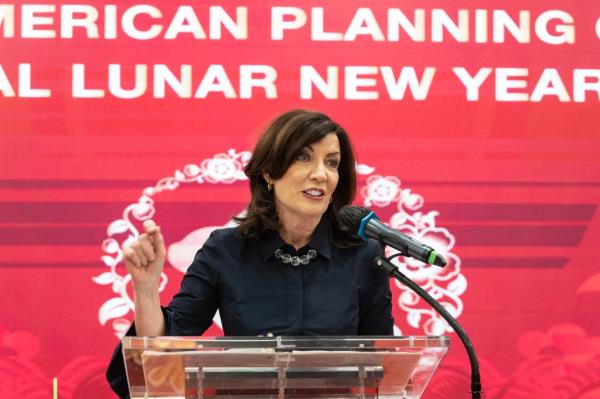 Hochul speaking at a dais in front of a lunar new year celebration banner in red