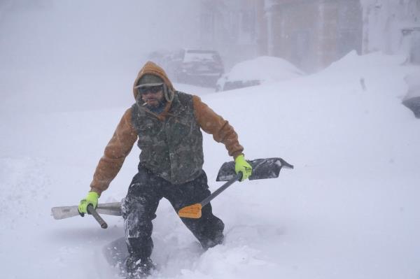 Travis Sanchez trudges over a snowdrift with a pair of shovels for a stranded motorist on Chenango Street in Buffalo, N.Y. on Saturday, Dec. 24, 2022