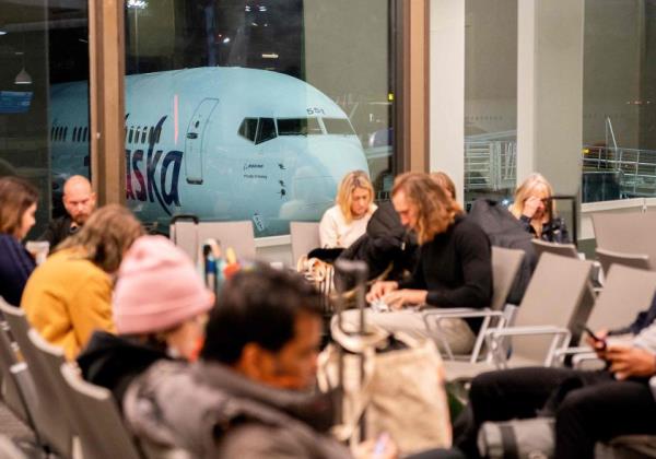 Travelers wait in the terminal as an Alaska Airlines plane sits at a gate at Los Angeles Internatio<em></em>nal Airport.