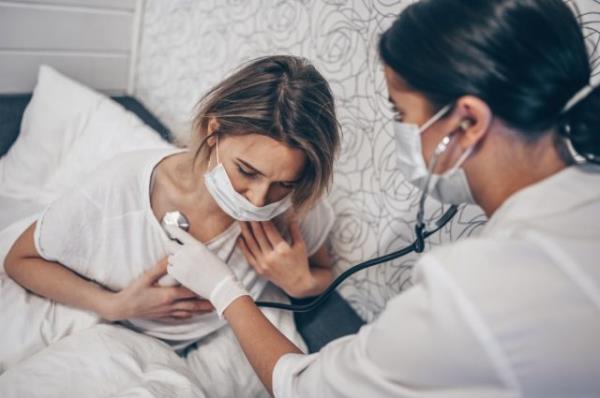 Doctor nurse in protective face mask listening to breath with a stethoscope suspecting Coro<em></em>navirus (COVID-19).