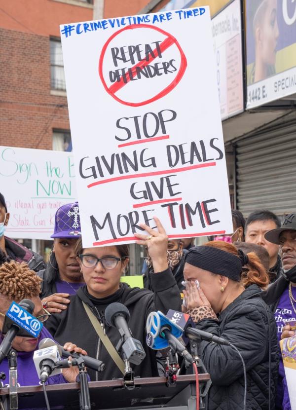 A protest sign with the phrase repeat offenders crossed out being held by a person in an outdoor crowd