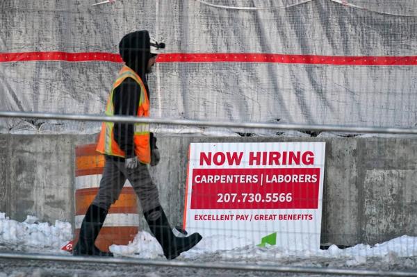 A co<em></em>nstruction worker walks past a job site advertising openings