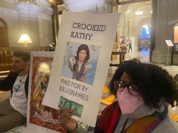 A protestor holding a sign criticizing Gov. Hochul for taking do<em></em>nations from billionaires. 