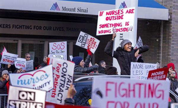 A supporter stands through the sunroof of a passing vehicle in front of Mt. Sinai Hospital in the Manhattan borough of New York Monday, Jan. 9, 2023, as nurses stage a strike following the breakdown of negotiations with the hospital hours earlier.
