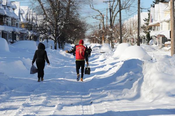 Pedestrians make their way through snow covered streets after an intense lake-effect snowstorm that impacted the area on November 20, 2022 in Buffalo, New York. 
