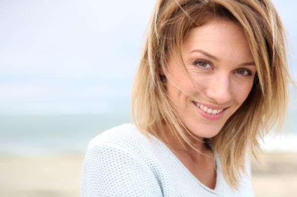 Close-up portrait of a smiling middle-aged woman with dirty blo<em></em>nde hair on the beach