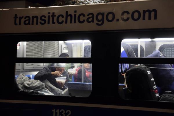 Outside the Chicago police 1st District station, migrants eat and take a break from the cold weather on a Chicago Transit Authority warming bus on Oct. 30, 2023. 