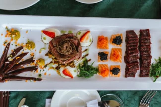 A long plate seen from above, with sushi-like morsels of meat and fish laid out on it 