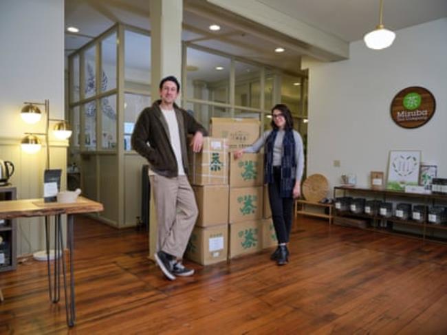 A man and a woman in a work/warehouse space with boxes of product.
