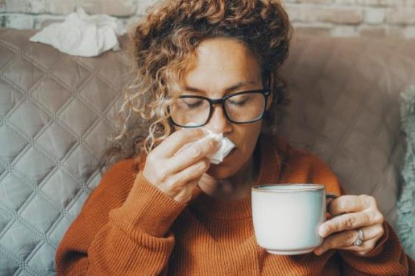 Sick woman at home blowing nose and take care of influenza virus disease. One female people using paper tissue and drink herbal tea medicine alone at home. Co<em></em>ncept of flu cold in winter season indoor