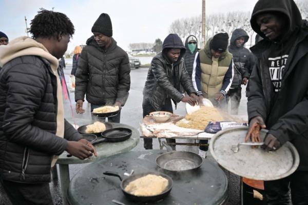 Sudanese migrants preparing a typical Sudanese meal with tuna, water and flour provided by charity associations, in a migrant camp, in Ouistreham, northwestern France on December 11, 2022. | Photo: LOU BENOIST/AFP