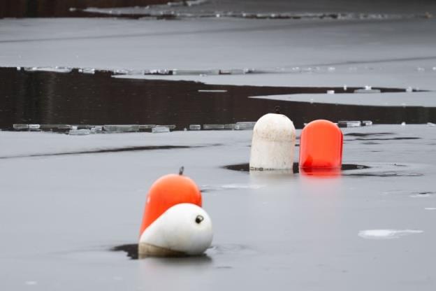 Orange and white buoys on a body of water with thin ice and open water.