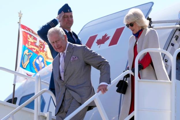 Two people exit from an airplane as a person saluting stands in the background.