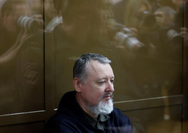 A man with a goattee sits in a court dock with a reflective look on his face.