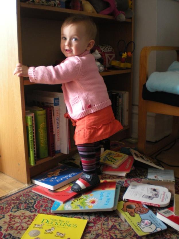 A toddler standing on a small pile of books on the floor.