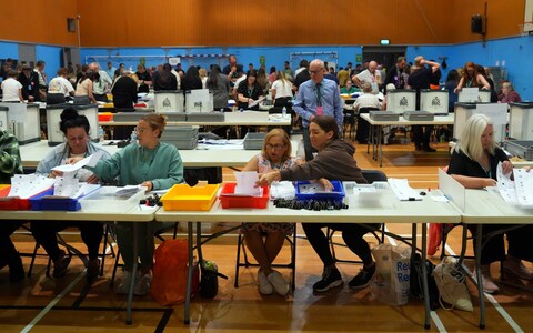 Counters stack voting slips into red, blue, yellow and white plastic trays
