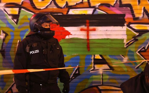 A riot policeman stands next to a graffiti-covered wall that shows a Palestinian flag during a gathering of pro-Palestinian demo<em></em>nstrators in Neukoelln, Berlin