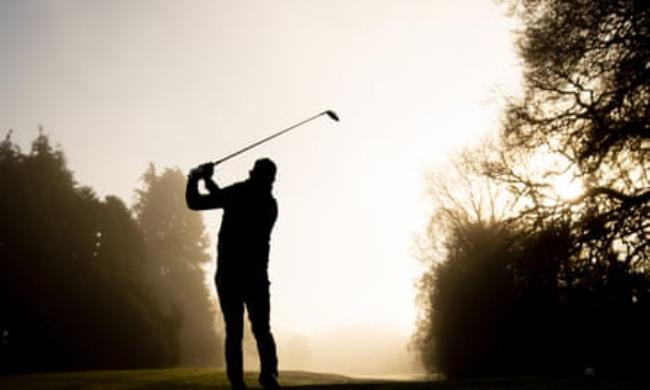 A golfer swinging his club against a backdrop of trees