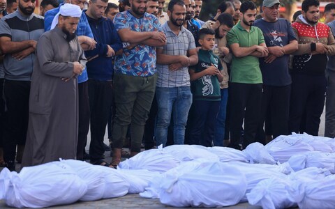 Palestinians pray by the bodies of relatives killed following Israeli bombardment, at Al-Aqsa hospital