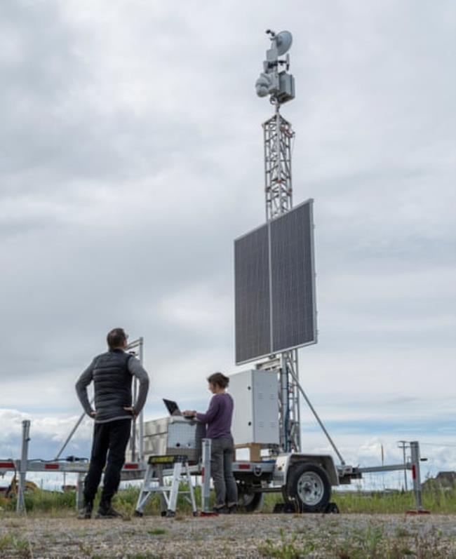 A man looks up at a solar panel-operated radar tower