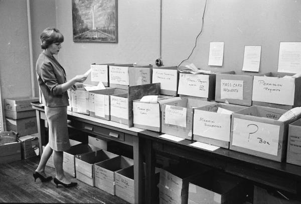 A woman in the 1960s standing in front of a table filled with boxes to categorise letters