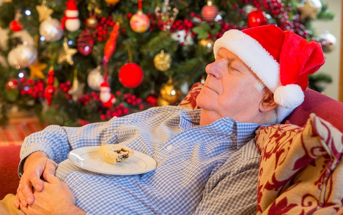 A tired grandfather sleeps on the sofa with a mince resting on his belly