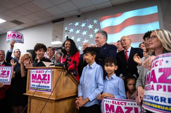 Mazi Pilip at a podium surrounded by supporters.