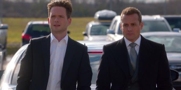 Mike Ross (Patrick J. Adams) and Harvey Specter (Gabriel Macht) sitting on the hood of a car in Suits.