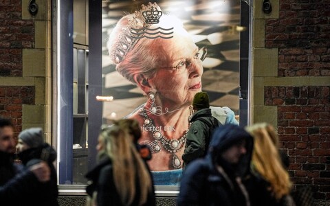 People pass a picture of Queen Margrethe II displayed in a window on a shopping street in Copenhagen
