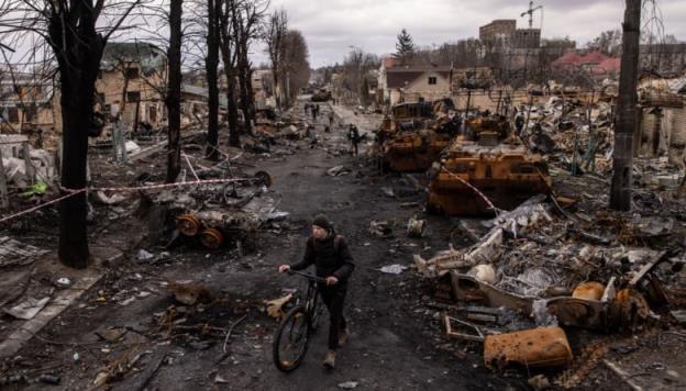 BUCHA, UKRAINE - APRIL 06: A man pushes his bike through debris and destroyed Russian military vehicles on a street on April 06, 2022 in Bucha, Ukraine. The Ukrainian government has accused Russian forces of committing a 