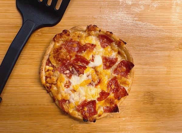 a single pepperoni pizza on a cutting board with a black spatula.