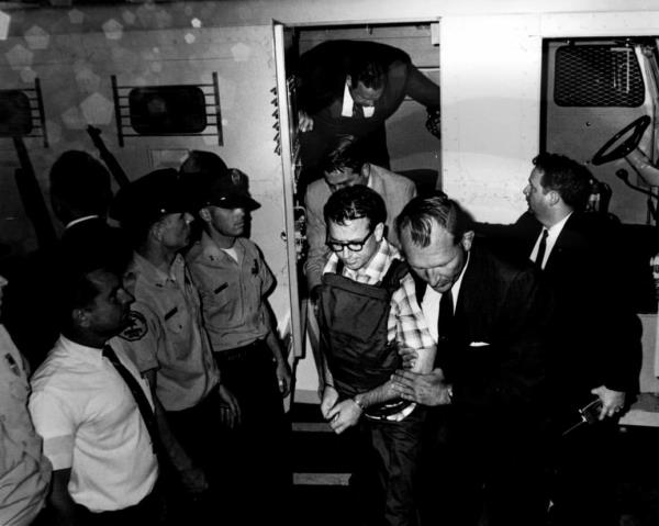 Lee Harvey Oswald handcuffed between two uniformed police