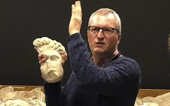 Dr Higgs holds a sculpted head and gestures, apparently while giving a talk