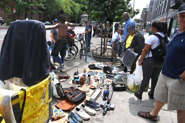 Crowd of people gathered around spread of wares being sold by illegal street vendors 