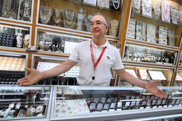 Man frowning with arms spread out behind counter of jewelry store