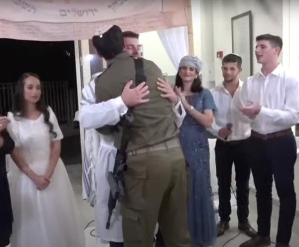 Yakir Abelow hugging the rabbi, clad in fatigues and strapped with a gun, at his wedding as others look on