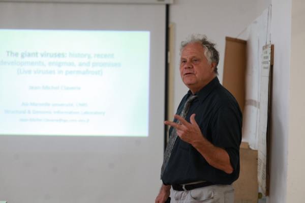 a geneticist named Jean-Michel Claverie standing on a stage with a projector screen in the background