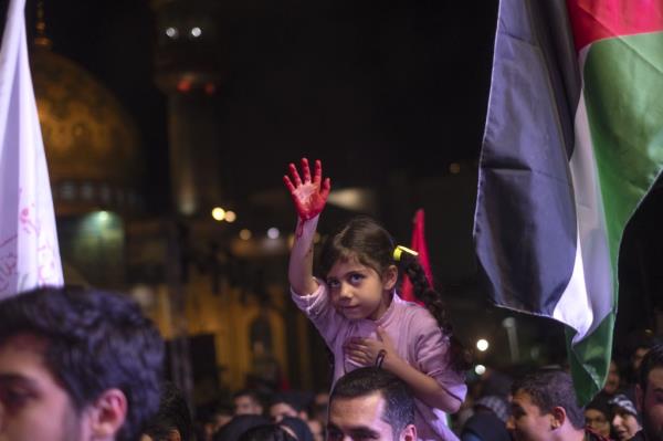 A young Iranian girl carried by her father holds-up her painted hand symbolizing the blood of Palestinian children, in downtown Tehran, Oct. 20.