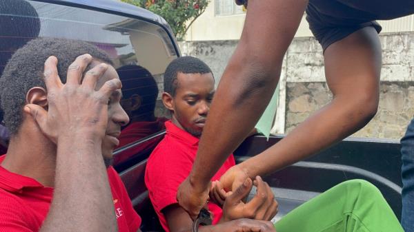 Two men in handcuffs sitting in the back of a truck in Kingstown, St. Vincent, suspected of hijacking a catamaran and murder.