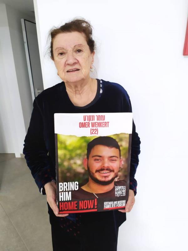 Tsili Wenkert holding a poster showing her grandson Omer Wenker's face and the words 