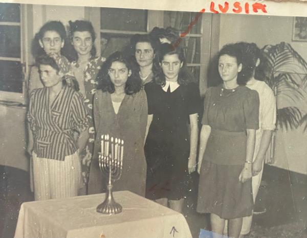 Teenage Lucy Lipiner with a group of other girls standing next to a table topped with a menorah