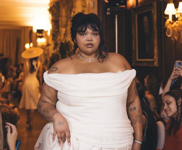 Moe Black poses on runway in white dress.